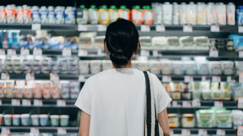 A woman in a white shirt looking at supermarket shelves filled with dairy products