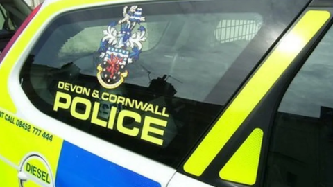 The side window of a Devon and Cornwall police care displaying a force logo and the words "Devon & Cornwall Police" 