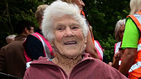 Grace Chambers smiling at the camera, she has white hair. People are standing behind her.