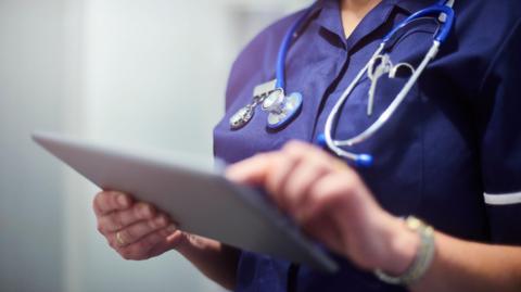 A nurse with a stethoscope holds a clipboard