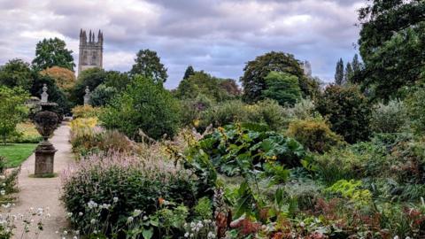 Gardens with luscious greenery dominates the image, with a spire in view in the background. 