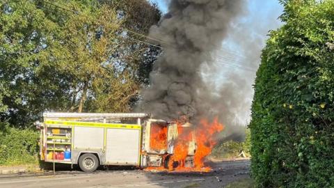 Fire engine caught ablaze on the side of a country road.