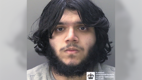 Custody photograph of a young man with long dark hair and a full beard looking directly at the camera, issued by Counter Terrorism Policing Wales.