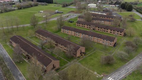 An aerial picture of MDP Wethersfield. There are seven blocks of accommodation, which are two-storeys. There are grassy areas and trees.