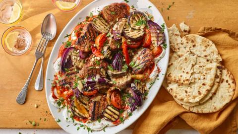 A white oval plate filled with grilled veg and lamb next to some torn flatbreads