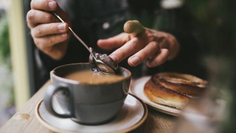 A tea drinker removes the tea bag from their cup.