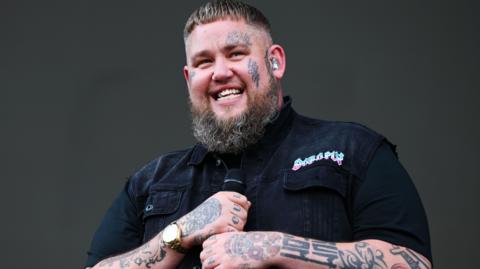 Rag'n'Bone Man performing at 91ȱ Radio 1's Big Weekend. He is smiling and holding a microphone.