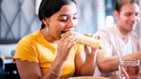 Woman eating a burrito in a restaurant