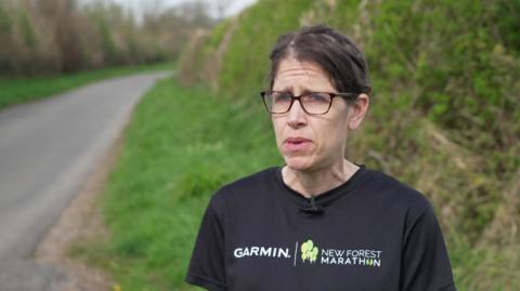 Heather Davey in a black Garmin t-shirt stood at the side of a road with green hedges and grass behind her.
