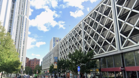 A large multi-storey car park in grey with a criss cross pattern exterior. The building is on a city centre street.