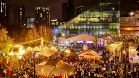 Fairy lights and brightly-lit stalls and a marquee can be seen along with crowds of people at the Christmas market.