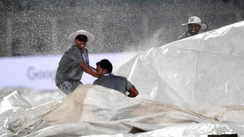 Groundstaff attempt to cover outfield with covers