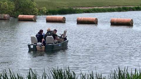 A small black boat on a river with three officers, dressed in black sat in it.