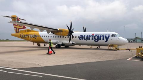 Aurigny plane in white and yellow livery, with blue writing, on a runway