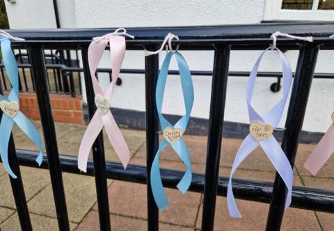 Blue, pink and lilac ribbons along a railing with white hearts in the middle with names of babies written on them