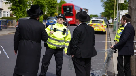 Body-worn footage showing a police officer's arm holding a Taser, another officer to the left and the knife suspect walking towards them