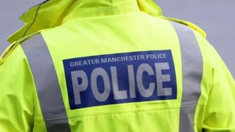close up of the back of a high vis yellow police coat with "Greater Manchester Police" on the back in blue