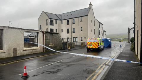 Police van and police tape on road at scene of incident among houses