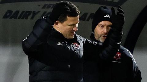 Exeter City  manager Gary Caldwell with his arms in the air on the touchline.