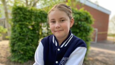 A young girl smiles into the camera while wearing a Leavers 2026 jumper.