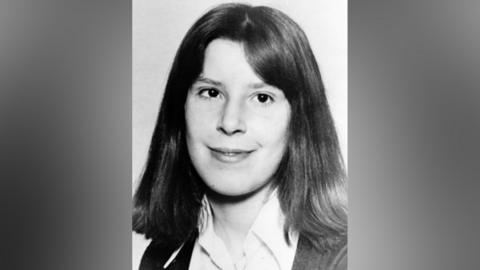A black and white image of Suzanne Lawrence, who has shoulder-length hair and wears a shirt and cardigan.