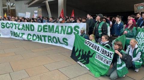 A large group of protesters hold up banners, saying Scotland demands rent controls, outside the Scottish Parliament