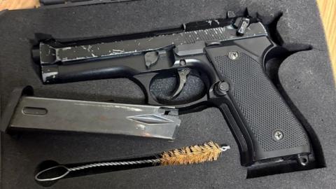 A black, automatic pistol, an ammunition magazine and a barrel cleaning brush in a foam case