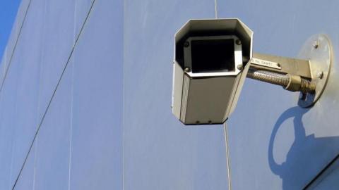 A silver CCTV camera is attached to a silver metal wall. 
