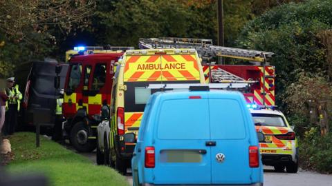 Several emergency service vehicles are parked on a country road. 