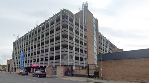 A concrete car park with several storeys and a blue car park sign.