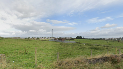 A GV exterior view of an overgrown field with some buildings in the background.