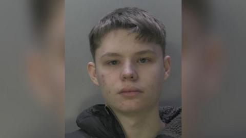 A mugshot of Thomas Waller. He is wearing a grey hooded top and looking at the camera.