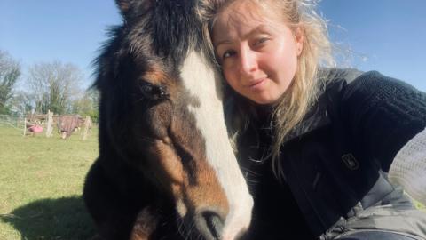 A woman posing for a photo with a brown and white horse while lying down.