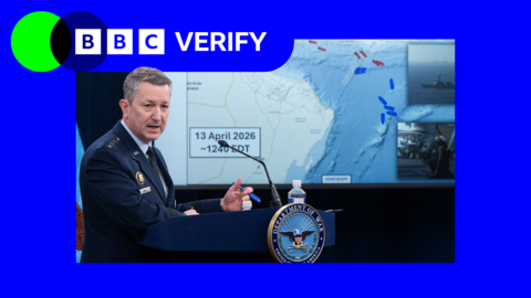 Gen Dan McCaine wearing a blue US Air Force uniform stands at a lectern in front of a screen showing a map of the Strait of Hormuz and the Gulf of Oman