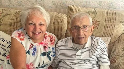 Jacqui Scott and Donald Sheppard smiling directly at the camera while sitting on a sofa