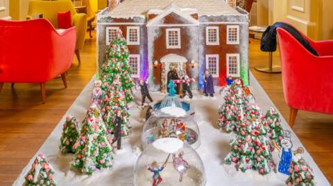 The gingerbread model shows a Georgian-style house topped with snow and decorated Christmas trees and two igloos in its snowy front garden, laid out on a table inside The Assembly House.