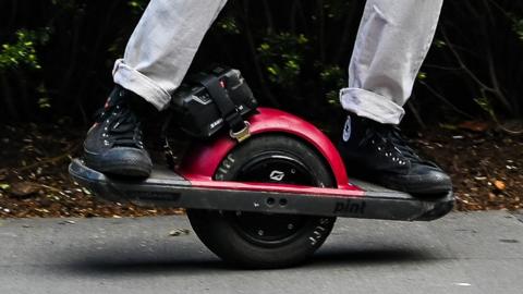 A Onewheel electric skateboard - a skateboard with a single wheel in the middle. The person stands either side of the wheel for balance.