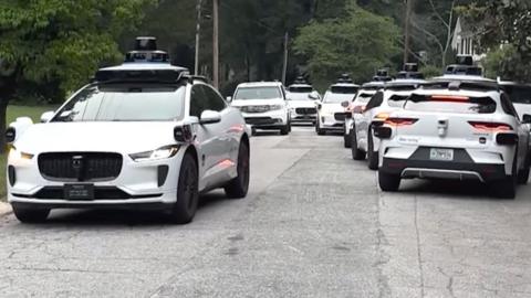 A litany of Waymo cars take up all the space in a street.