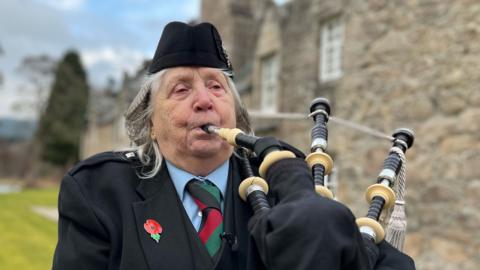 A woman wearing formal Highland dress playing the bagpipes