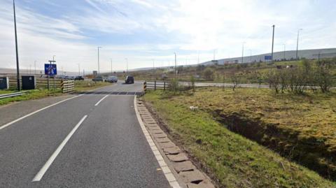 The end of a slip road off the M62 Junction 22 eastbound. Pictured is a cattlegrid with wooden fences either side.