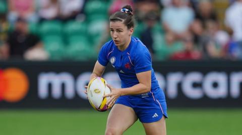 Gabrielle Vernier holds the rugby ball between two hands as she runs on the pitch during a World Cup 2025 match for France