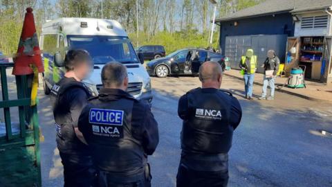 NCA officers watch as other officials and officers question staff at a industrial site