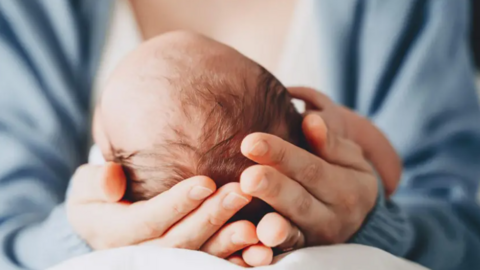 A mother holds a new born baby in her hands. She is wearing a blue top.