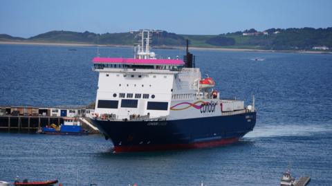 The Condor Islander, a boat with a blue bottom and a white top with the word Condor on the side, pulling into Guernsey's St Peter Port harbour on a calm still day. 