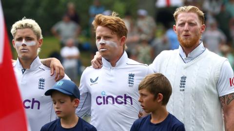 Ben Stokes stands beside Ollie Pope and Jacob Bethell