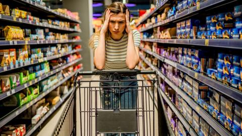 Woman holding her head in her hands next to shopping trolley
