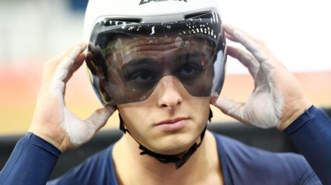 Matthew Richardson holds his hands to his helmet visor as he sits on the startline of a race