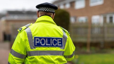 Police officer wearing a high vis jacket and walking around what looks like a housing estate