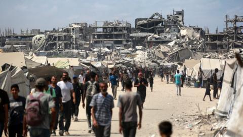 A crowd of Palestinian residents walk down a sandy street against the backdrop of destroyed buildings in Gaza City on Friday.