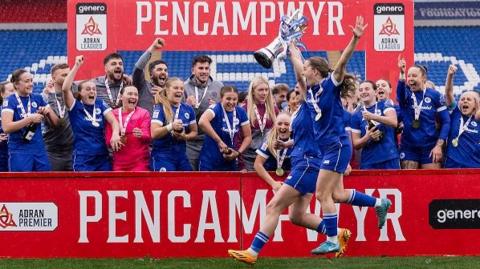 Cardiff City Womens' Fiona Barry Lisa Owen lift the Adran League trophy as team-mates and staff celebrate